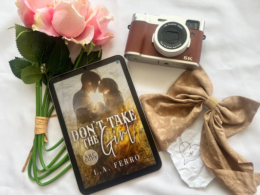 Don’t Take the Girl by L.A. Ferro with flowers, vintage camera, and romantic props on white background.